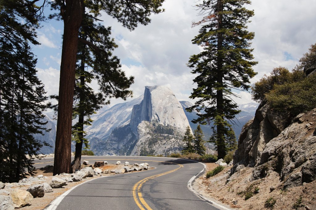 Trees part at the end of a road to show a view of Half Dome and Yosemite Park | My Dream Travel List - Part One | travelbloom.blog